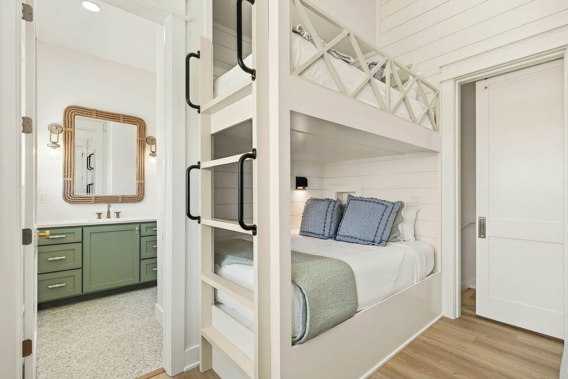 A bedroom with a bunk bed, a green dresser, a mirror with a rope frame, and a white door.