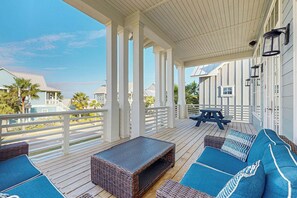 A covered outdoor deck with a seating area, including a table and chairs, and a view of the surrounding neighborhood. - Sunset Palms | Steps to Beach | Putting Green (Port Aransas)
