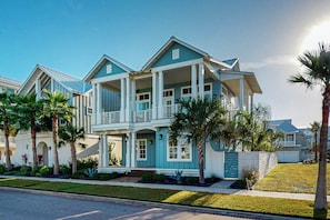 A two-story house with a balcony, surrounded by palm trees and a well-maintained lawn. - Sunset Palms | Steps to Beach | Putting Green (Port Aransas)