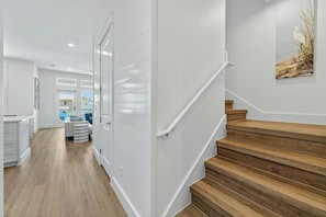 A modern interior with a wooden staircase, white walls, and a view into another room. - Sunset Shores Escape| Water Views | Steps to Beach (Port Aransas)