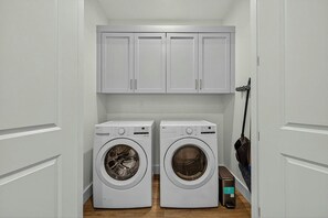Une buanderie équipée de deux machines à laver à chargement frontal, d’une serpillière et d’un meuble de rangement au-dessus.