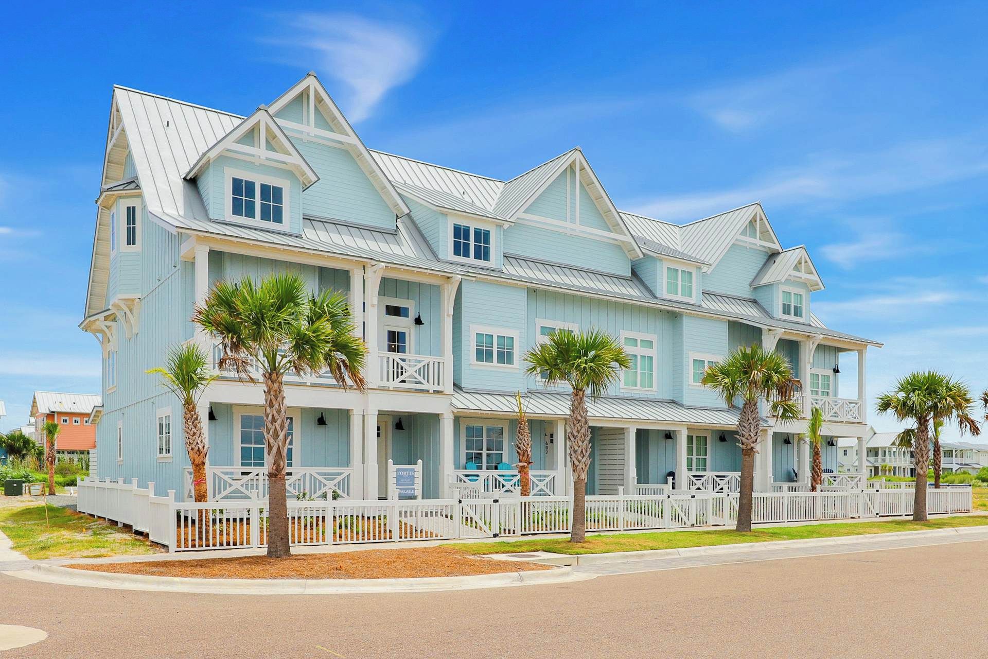 A large, multi-story building with a light blue exterior, white trim, and a white picket fence surrounding the property.