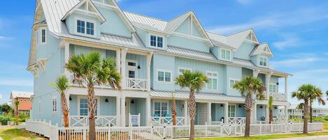 A large, multi-story building with a light blue exterior, white trim, and a white picket fence surrounding the property.