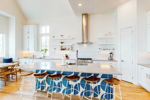 A modern kitchen with white cabinetry, a central island with bar stools, and a stainless steel range hood. - Sunshine Overtime | Water Views | Private Pool (Port Aransas)