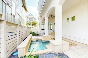 A residential courtyard with a swimming pool, a covered seating area, and a view of a neighboring building. - Sunshine Overtime | Water Views | Private Pool (Port Aransas)