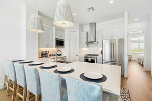 A modern kitchen with a large island, stainless steel appliances, and a dining area with striped chairs. - The Coral Monkey | Resort Amenities (Port Aransas)