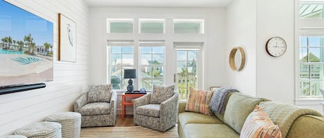 A living room with a large window, a sofa, two armchairs, a coffee table, and a painting on the wall.