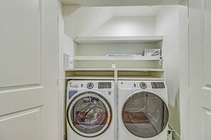 A laundry room with two front-loading washing machines and a shelf above them. - The Palm | Steps to Beach | Resort Amenities (Port Aransas)