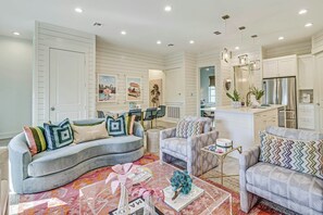 A modern living room with a curved grey sofa, a patterned armchair, and a coffee table with decorative items. - The Palm | Steps to Beach | Resort Amenities (Port Aransas)