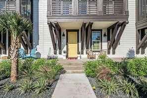 A two-story building with a yellow door, a covered porch, and a pathway leading to the entrance. - The Palm | Steps to Beach | Resort Amenities (Port Aransas)