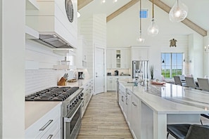 A spacious kitchen with a large island, white cabinetry, and modern appliances. - Pelican's Perch | Private Elevator | Putting Green (Port Aransas)
