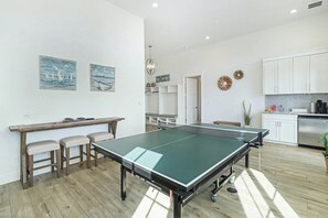 A ping pong table in a modern kitchen with white cabinets and a wooden floor. - Pelican's Perch | Private Elevator | Putting Green (Port Aransas)