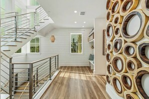 A multi-level interior with a staircase, wooden flooring, and a wall with circular wooden elements. - Palmilla Pearl-Tallest In Palmilla | Gulf Front (Port Aransas)