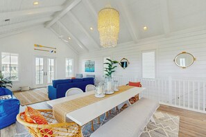 Ein geräumiges Wohnzimmer mit hoher Decke, einer Kandelaber, einem blauen Sofa, einem weißen Esstisch und einem weißen Geländer.