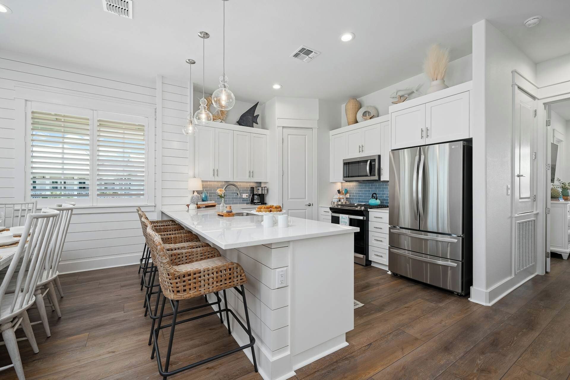 A modern kitchen with white cabinetry, a central island, bar stools, a stainless steel refrigerator, and a microwave.