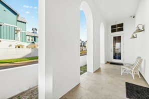 A covered porch with white columns, a door with glass panels, and a white chair. - Mermaid Dreams | Gulf Views | Private Elevator (Port Aransas)