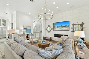 A spacious living room with a large sofa, a fireplace, and a chandelier. - Mermaid Dreams | Gulf Views | Private Elevator (Port Aransas)