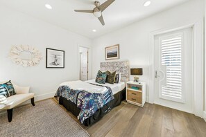 Quarto com cama, cadeira, mesa de cabeceira, abajur e porta com persianas.