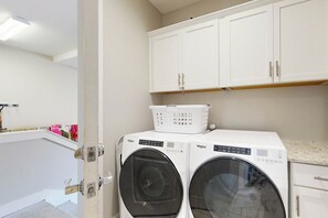 A laundry room with two front-loading Whirlpool washers, a white basket on top, and a wooden shelf above. - Gone Fishin | Pet Friendly | Steps to Beach (Port Aransas)