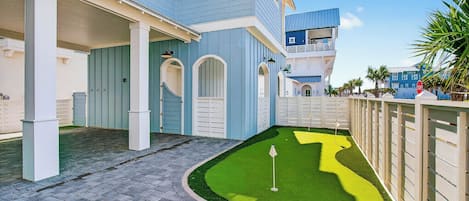 Une propriété résidentielle dotée d’une allée pavée, d’une petite pelouse avec un trou de golf et d’une entrée fermée par un portail.