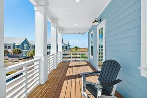 En træterrasse med en stol, hvide gelændere og udsigt til huse i baggrunden.