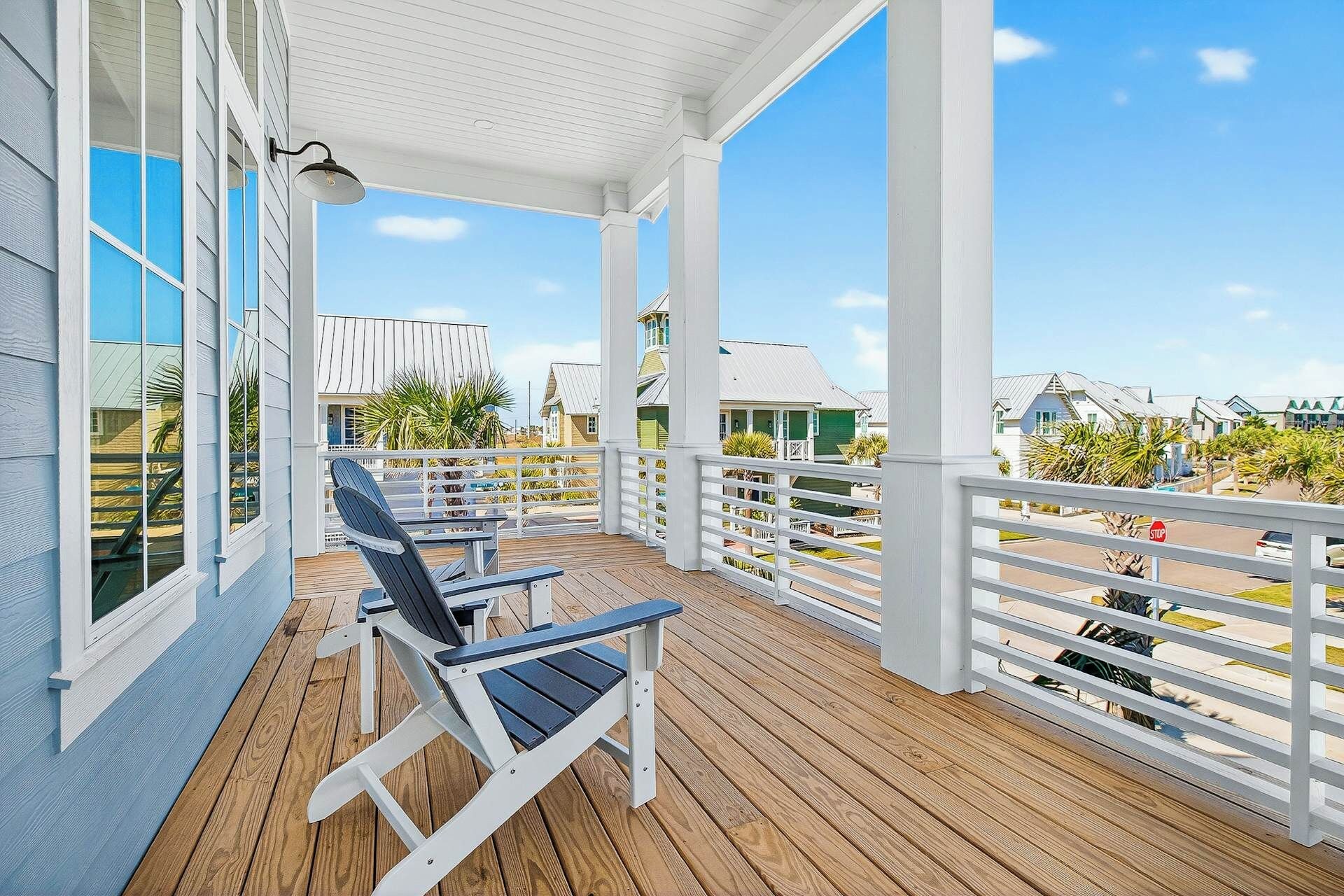 A covered wooden deck with white railings and a view of the beach and buildings in the background.