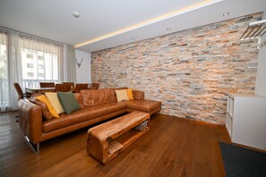 A modern living room with a brown leather sofa, wooden coffee table, and a stone wall. - Zell City Exclusive Lodges TOP 3 Balcony (Zell am See)