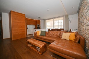 A modern living room with a brown leather sofa, wooden coffee table, and a kitchen area with white cabinets. - Zell City Exclusive Lodges TOP 3 Balcony (Zell am See)
