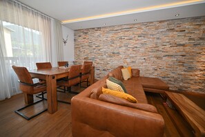 Un salon moderne avec un mur en pierre, un canapé en cuir, une table à manger et des chaises.