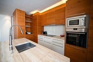 A modern kitchen with wooden cabinets, a stainless steel sink, a microwave, and an oven. - Zell City Exclusive Lodges TOP 3 Balcony (Zell am See)