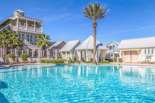 Ett poolområde med solstolar och en stor byggnad med en balkong.