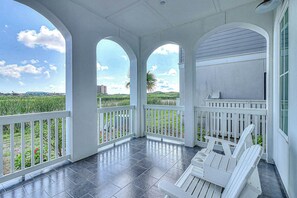 A covered porch with a view of a green landscape and a building in the distance. - Cattail Castle | Water Views | Steps to Beach (Port Aransas)