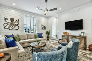 A modern living room with a sofa, armchairs, a coffee table, and a television. - Casitaville | Steps to Beach | Resort Amenities (Port Aransas)