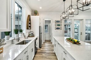 A modern kitchen with white cabinetry, a central island, and a wooden floor. - Casitaville | Steps to Beach | Resort Amenities (Port Aransas)