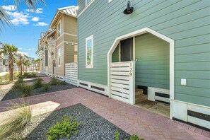 A charming coastal-style entrance welcomes you with soft mint-green siding and palm trees swaying in the breeze. - Casitaville | Steps to Beach | Resort Amenities (Port Aransas)