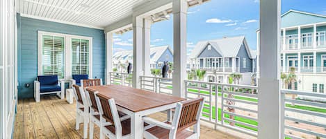 A covered outdoor area with a wooden deck, white chairs, and a table.