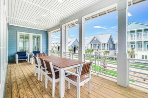 A covered outdoor area with a wooden deck, white chairs, and a table. - 'Merica Estate | Steps to Beach | Game Room (Port Aransas)