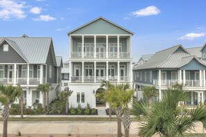 A multi-story residential building with a balcony on the second floor, surrounded by palm trees and a clear sky. - A Wave From It All | Gulf Views | Steps to Beach (Port Aransas)