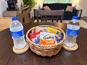 Ein Esstisch mit einem gewebten Korb, der Snacks, zwei Wasserflaschen und eine Packung Goldfish-Cracker enthält.