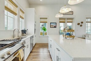 A modern kitchen with a large island, stainless steel appliances, and a view of the city. - Casitas Sweetbay| Resort Amenities |Steps to Beach (Port Aransas)