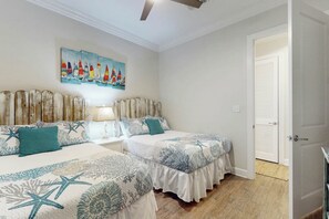 Ein Schlafzimmer mit zwei Betten, einem Nachttisch, einer Lampe, einem Segelbootgemälde und einem Holz-Kopfteil.