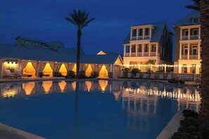 Nattebillede af et hotel med swimmingpool, palmer og bygninger med varm belysning.