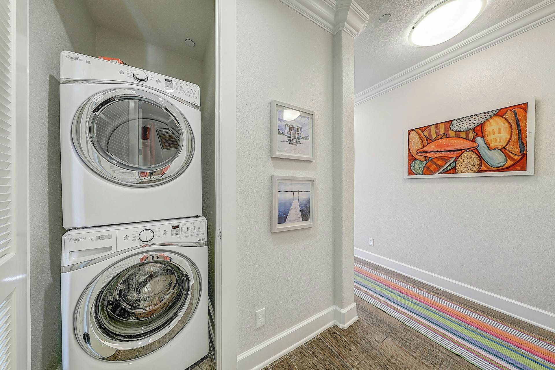 Ein Waschraum mit zwei übereinander gestapelten Whirlpool Trocknern, einem gerahmten Gemälde an der Wand und einem Streifen Teppichboden.