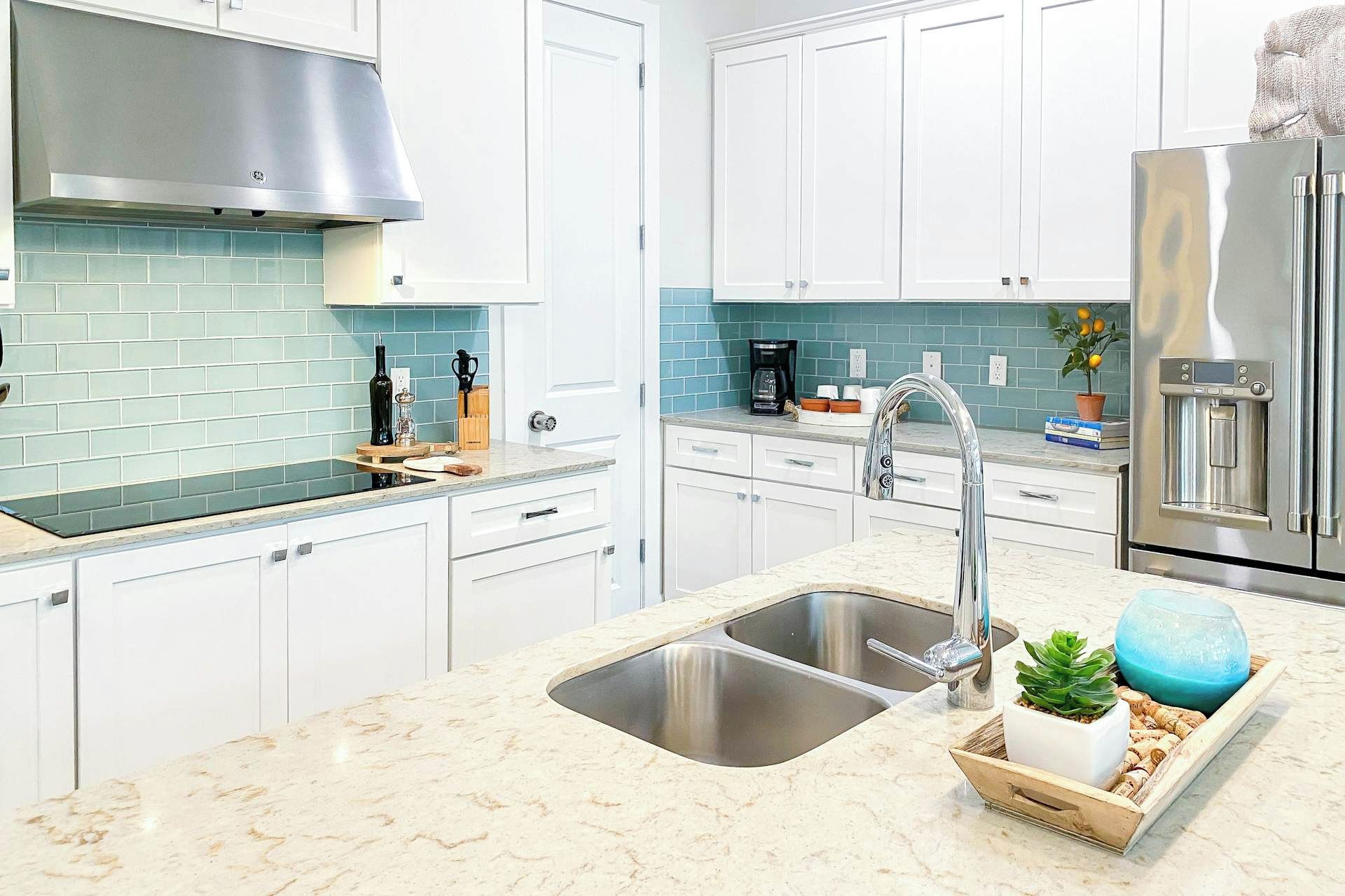 Una cocina moderna con armarios blancos, una campana extractora de acero inoxidable, un lavamanos doble y un refrigerador empotrado.