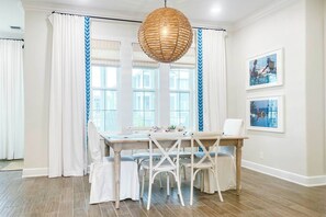 A dining area with a wooden table, white chairs, and a woven pendant light. - Family Tides | Steps to Beach| Resort Amenities (Port Aransas)