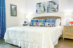 A hotel room with a large bed, two bedside tables, a nightstand, a lamp, a vase with flowers, and abstract art on the wall. - Family Tides | Steps to Beach| Resort Amenities (Port Aransas)