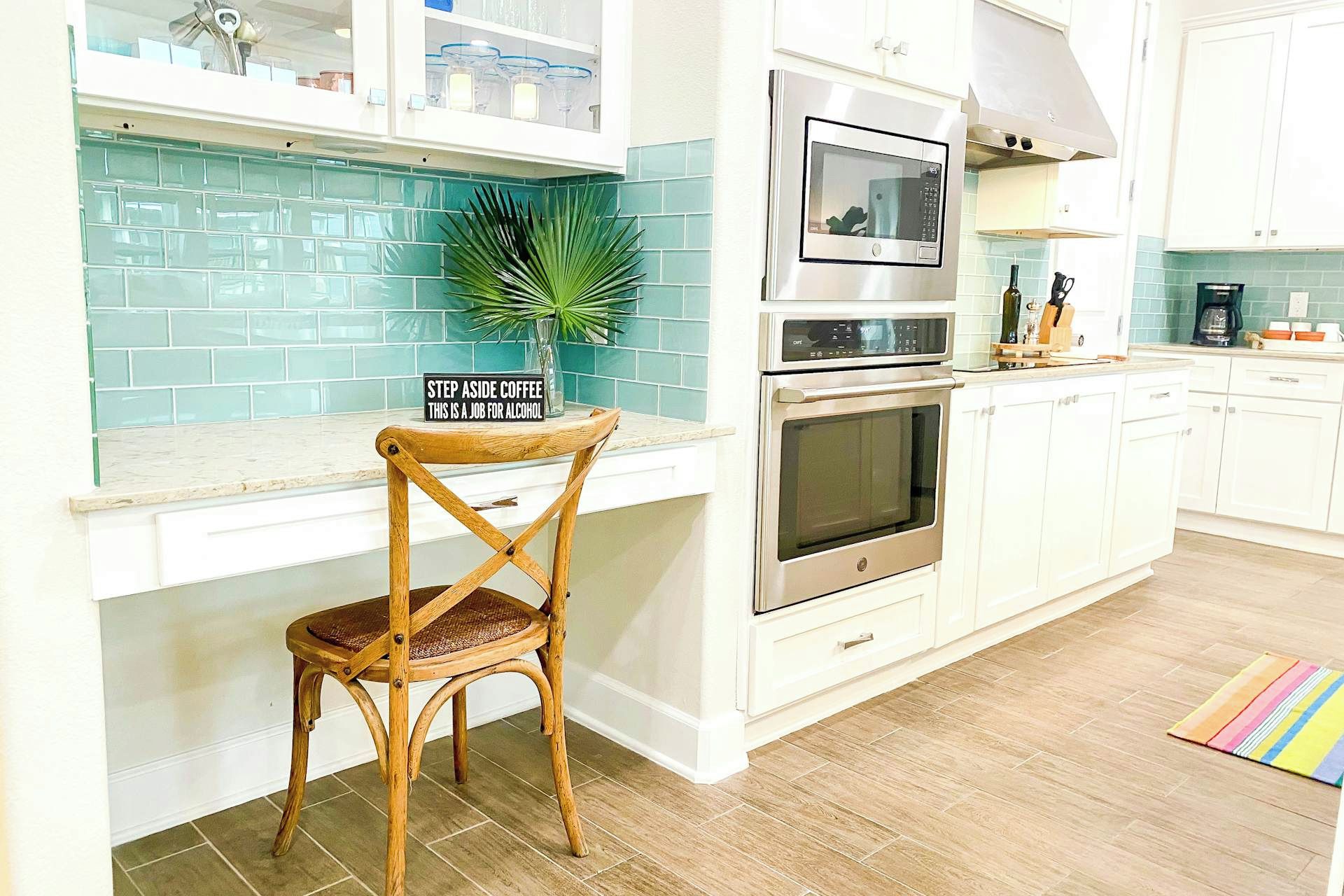 Una cocina con armarios blancos, microondas, horno y una silla de madera con un letrero.
