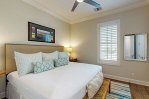 A hotel room with a large bed, a ceiling fan, a framed picture on the wall, a window with blinds, and a mirror. - Birdie Beach | Steps to Beach | Resort Amenities (Port Aransas)