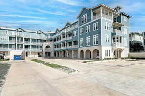 A multi-story hotel with a central courtyard, balconies, and a parking area. - Birdie Beach | Steps to Beach | Resort Amenities (Port Aransas)