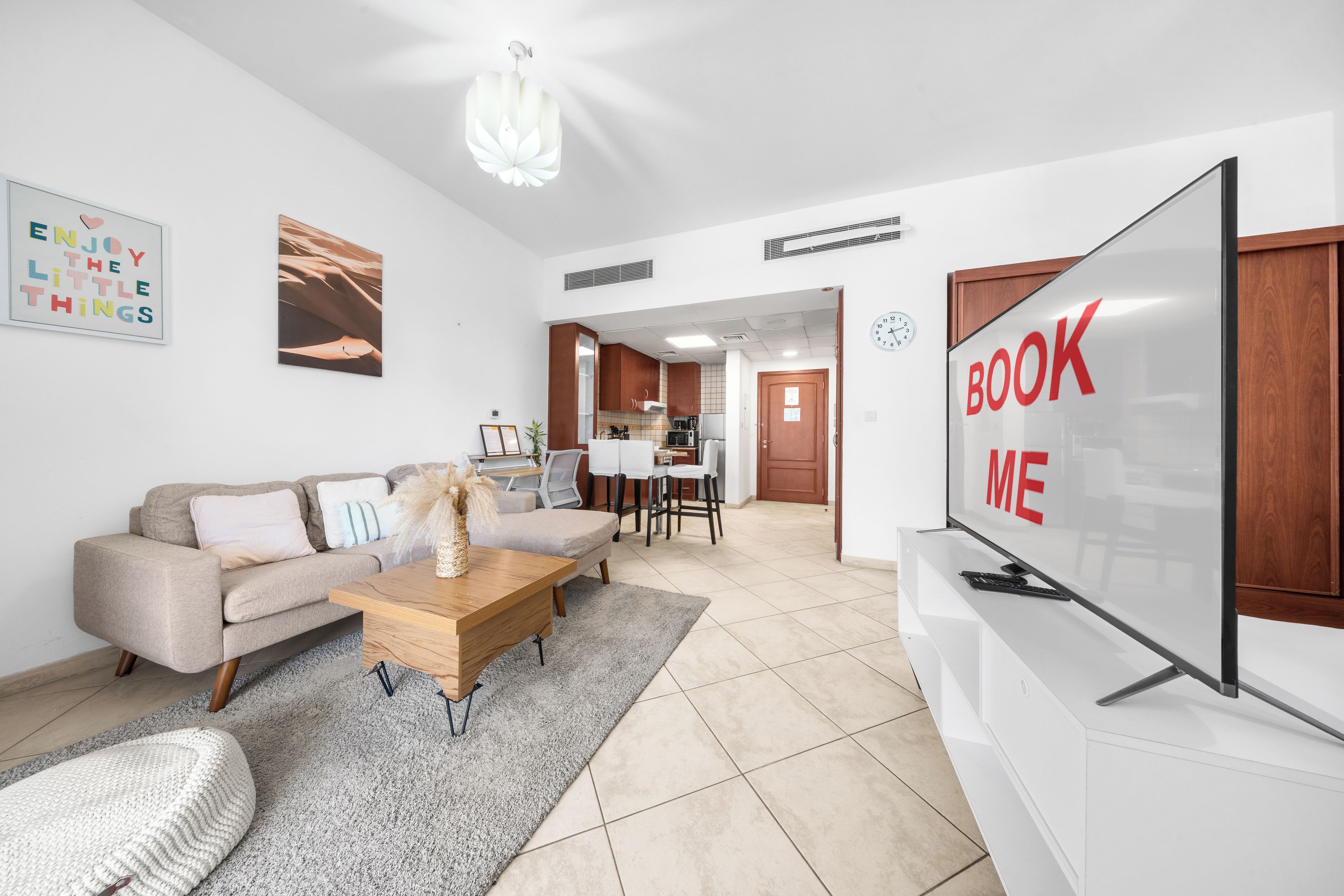 A modern living room with a sofa, coffee table, and a TV screen displaying 'BOOK ME'.